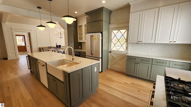 kitchen with a sink, decorative backsplash, light wood-type flooring, high quality fridge, and light countertops