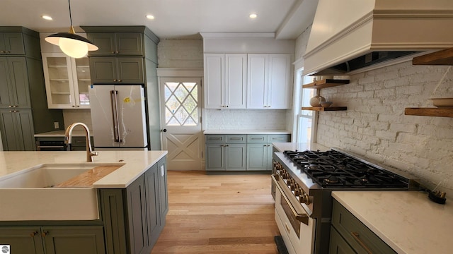kitchen featuring green cabinetry, open shelves, premium appliances, and a sink