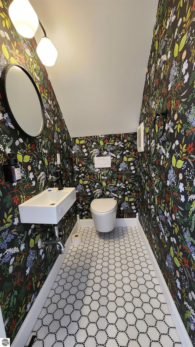 half bathroom featuring wallpapered walls, lofted ceiling, toilet, a sink, and baseboards