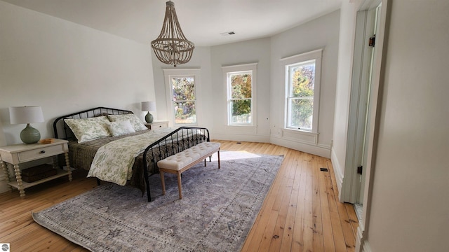 bedroom with a notable chandelier, multiple windows, and light wood-style floors