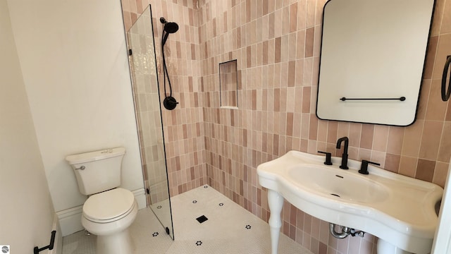 bathroom featuring tile walls, toilet, a sink, and tiled shower