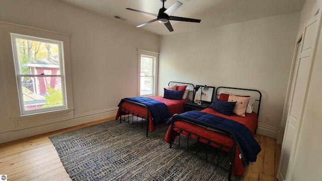 bedroom featuring wood-type flooring, visible vents, baseboards, and ceiling fan