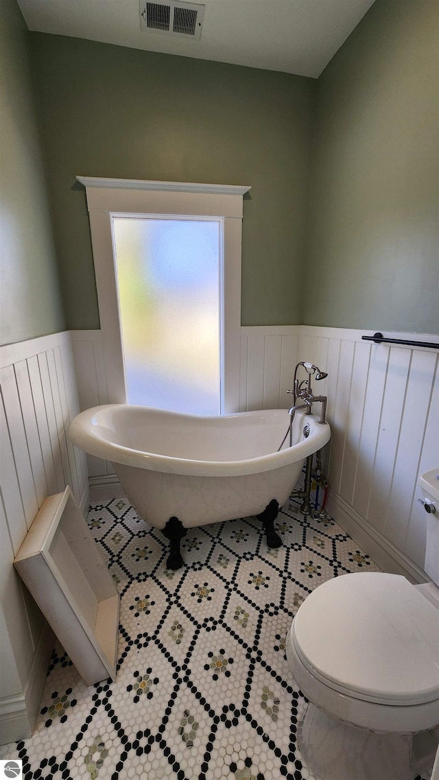 full bath with a soaking tub, toilet, a wainscoted wall, and visible vents