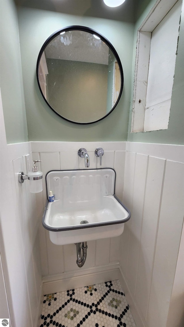 bathroom with wainscoting, a sink, tile patterned flooring, and a decorative wall