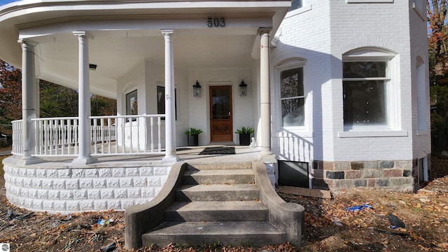 view of exterior entry with brick siding and a porch