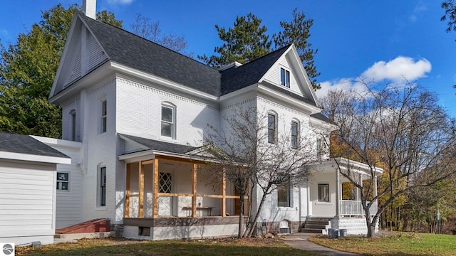 victorian-style house with a porch, a shingled roof, a chimney, and brick siding