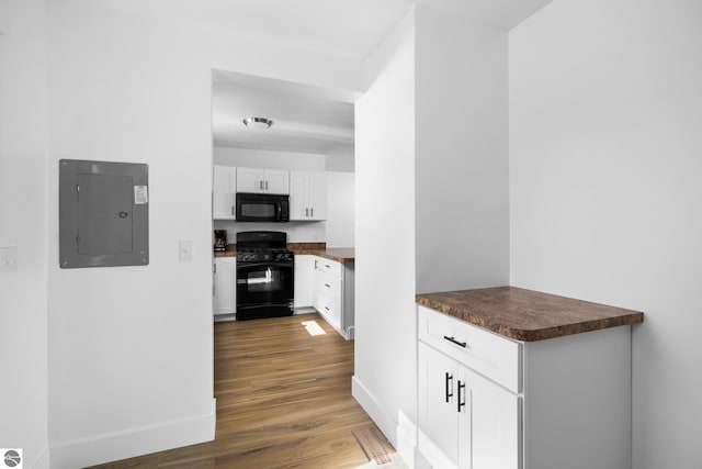 419 S Cherry St, Kalkaska, MI 49646 - kitchen with dark countertops, wood finished floors, black appliances, electric panel, and white cabinetry
