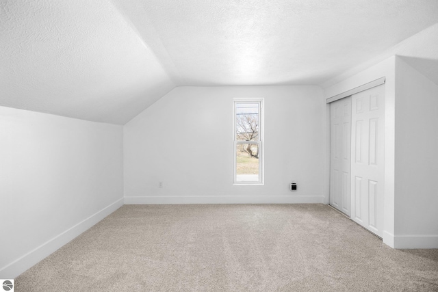 419 S Cherry St, Kalkaska, MI 49646 - additional living space featuring lofted ceiling, baseboards, a textured ceiling, and light colored carpet