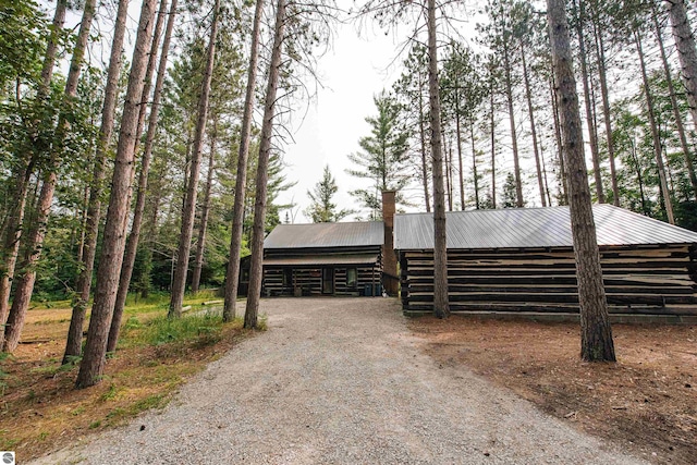 view of front of home with log exterior, an outbuilding, a chimney, and metal roof