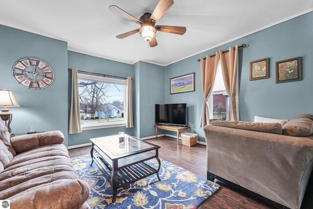 living area with baseboards, ornamental molding, a ceiling fan, and wood finished floors