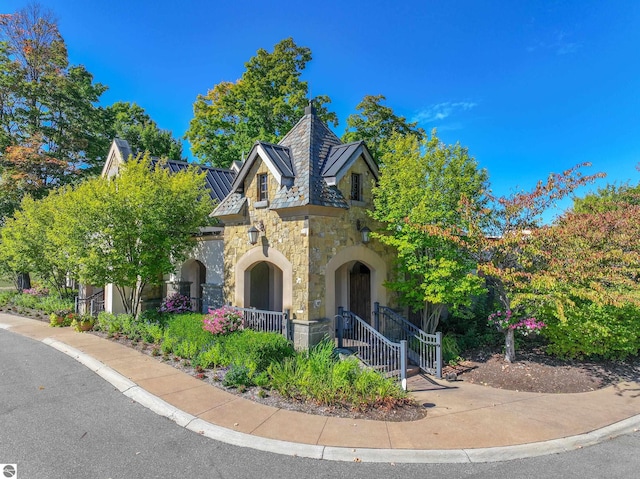 english style home with stone siding, a standing seam roof, metal roof, and a gate
