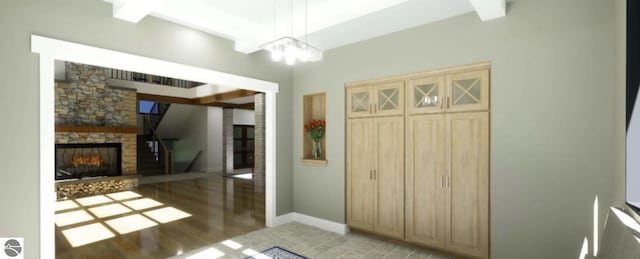 foyer entrance with light wood-style flooring, a chandelier, a stone fireplace, and baseboards