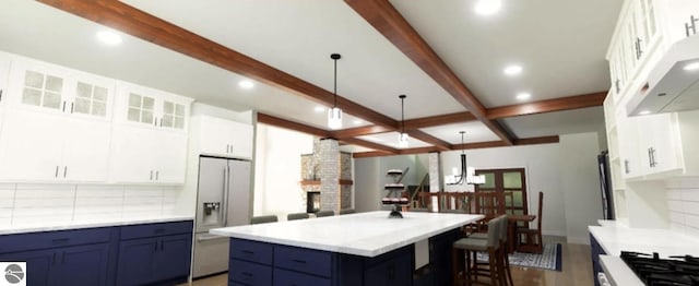 kitchen featuring stainless steel refrigerator with ice dispenser, blue cabinets, beamed ceiling, decorative backsplash, and light countertops
