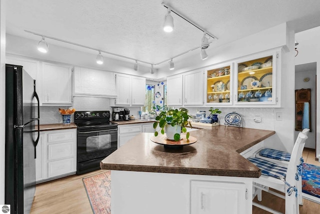 kitchen featuring white cabinets, a peninsula, light wood-type flooring, dark countertops, and black appliances