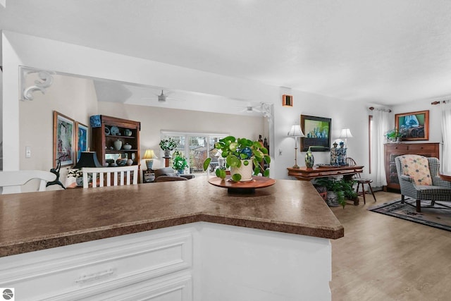 kitchen with dark countertops, open floor plan, ceiling fan, light wood-style flooring, and white cabinets