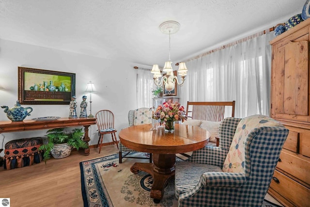 dining room featuring wood finished floors, a textured ceiling, baseboards, and an inviting chandelier
