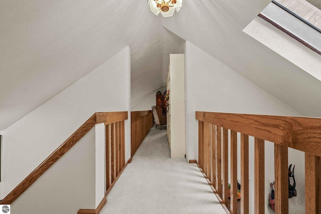hallway featuring light carpet, an upstairs landing, and vaulted ceiling with skylight