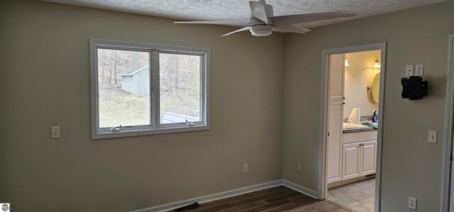 unfurnished bedroom with a textured ceiling, baseboards, multiple windows, and wood finished floors