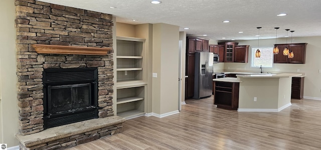 kitchen with a stone fireplace, light wood-type flooring, light countertops, baseboards, and stainless steel appliances