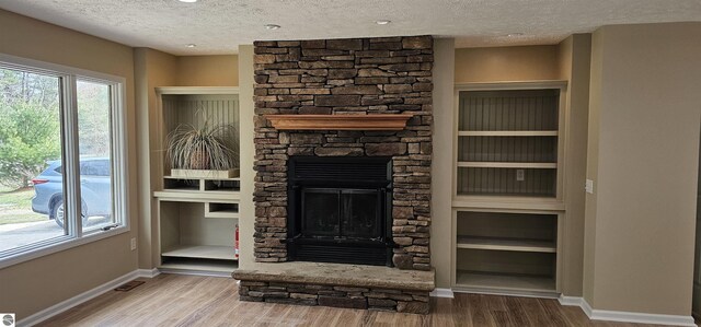 unfurnished living room with baseboards, a textured ceiling, wood finished floors, and a stone fireplace