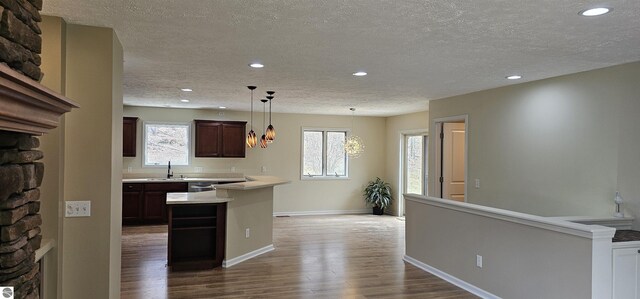 kitchen with a textured ceiling, a stone fireplace, a sink, light countertops, and recessed lighting