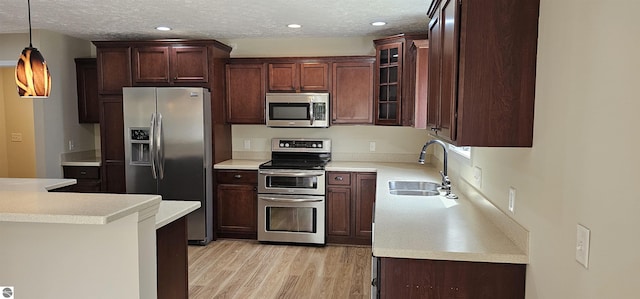 kitchen with appliances with stainless steel finishes, hanging light fixtures, a sink, light countertops, and light wood-style flooring