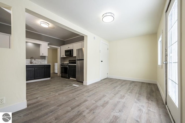kitchen featuring a sink, light wood-type flooring, light countertops, baseboards, and appliances with stainless steel finishes