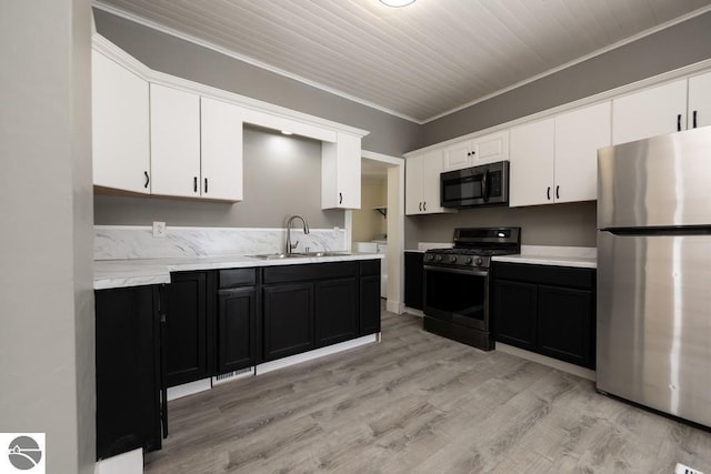 kitchen with a sink, freestanding refrigerator, white cabinetry, range with gas stovetop, and dark cabinets