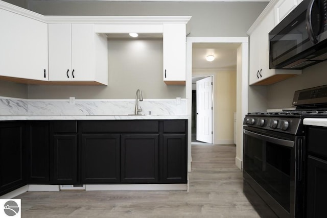 kitchen with gas range oven, white cabinets, black microwave, and light countertops