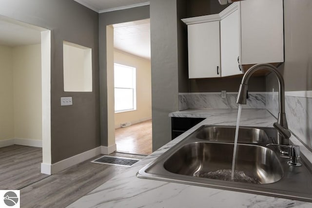 kitchen with white cabinets, wood finished floors, a sink, crown molding, and baseboards
