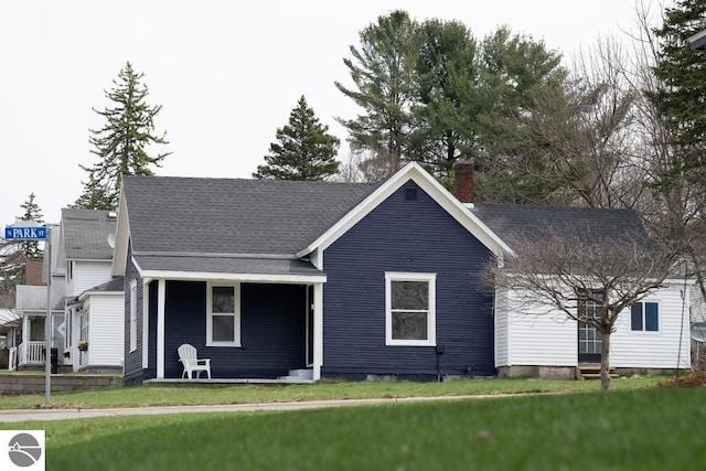 view of front facade featuring a chimney, covered porch, and a front yard