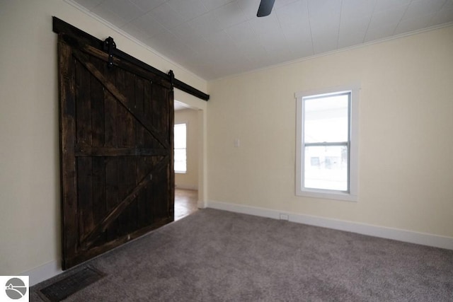 carpeted spare room with a barn door, baseboards, visible vents, a ceiling fan, and crown molding