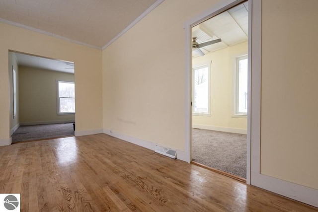 empty room featuring wood finished floors, visible vents, baseboards, and ornamental molding