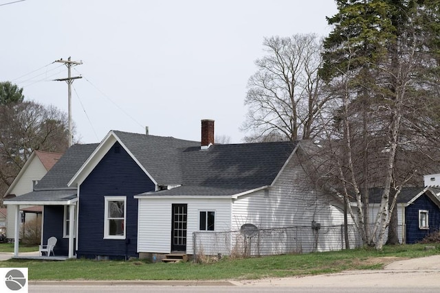 view of front of house featuring a chimney, entry steps, a shingled roof, and a front yard