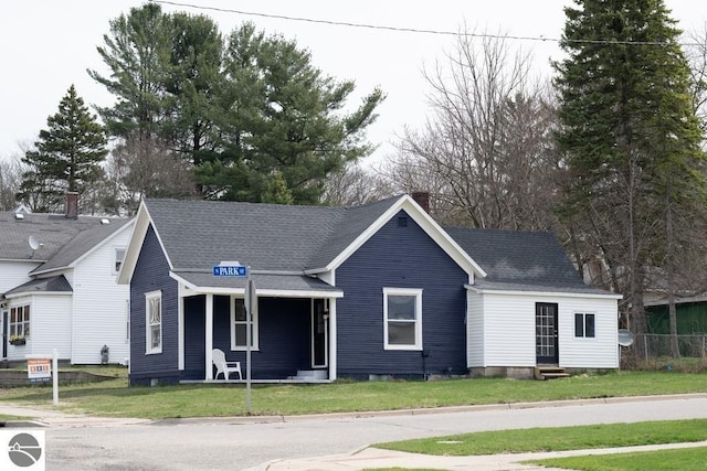 view of front of house with entry steps, a shingled roof, a front yard, and covered porch