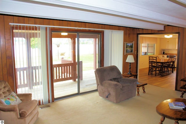 living room featuring beamed ceiling, visible vents, wood walls, and plenty of natural light