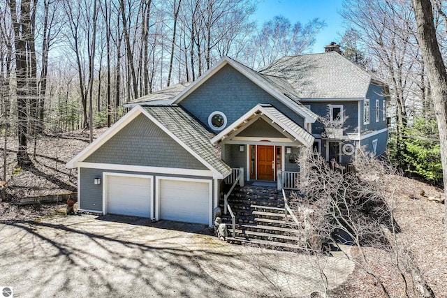1995 San Marino Trl, Kewadin, MI 49648 - view of front of house featuring a garage, a chimney, a shingled roof, and driveway