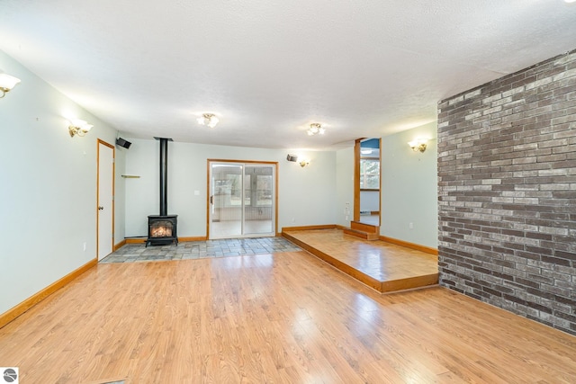 7888 E Broomfield Rd, Mount Pleasant, MI 48858 - unfurnished living room with a wood stove, baseboards, brick wall, and light wood-style floors