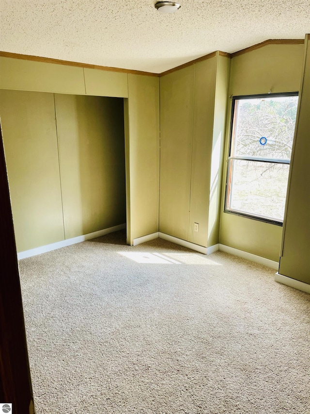 empty room featuring a textured ceiling, light colored carpet, ornamental molding, and baseboards
