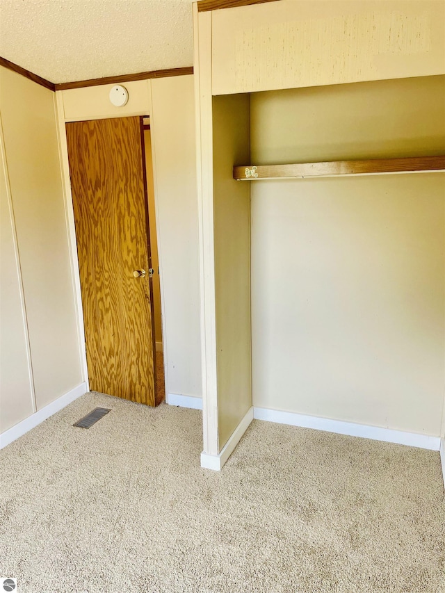 unfurnished bedroom with a textured ceiling, visible vents, a closet, baseboards, and carpet floors