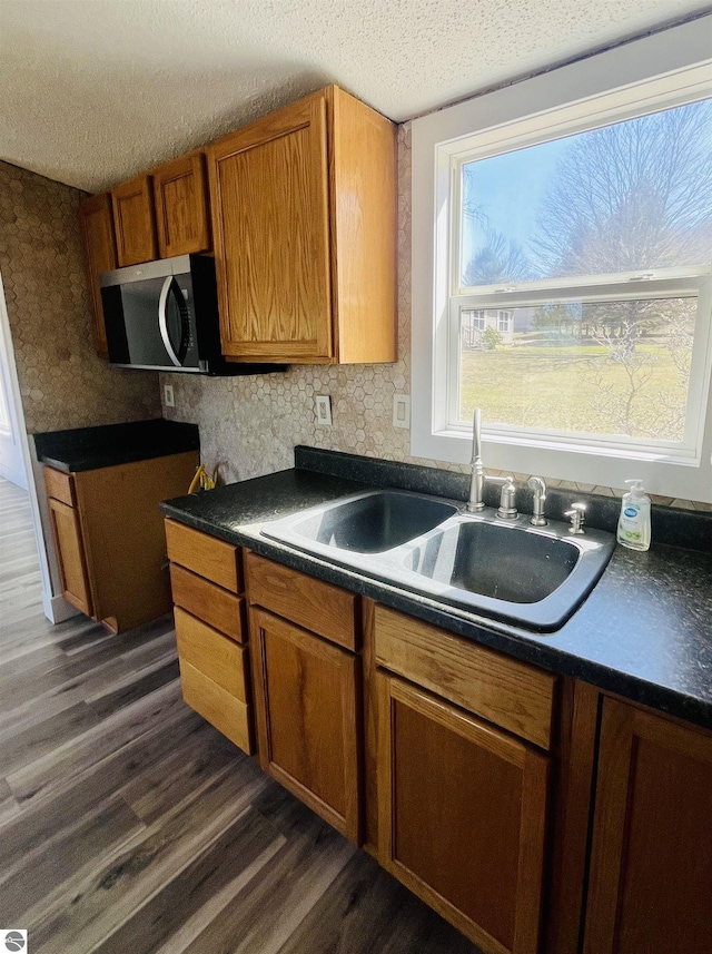 kitchen featuring stainless steel microwave, a sink, dark wood-type flooring, dark countertops, and a textured ceiling