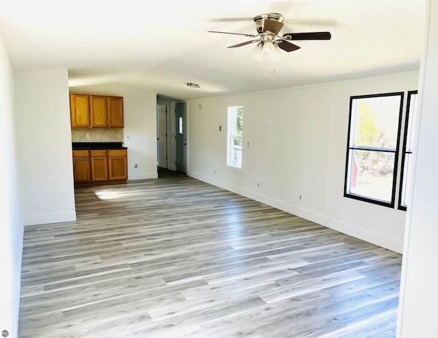 unfurnished living room with lofted ceiling, ceiling fan, baseboards, and light wood-style floors
