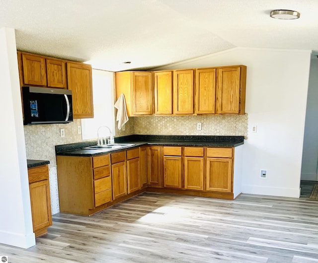 kitchen with stainless steel microwave, light wood-style flooring, a sink, brown cabinetry, and backsplash