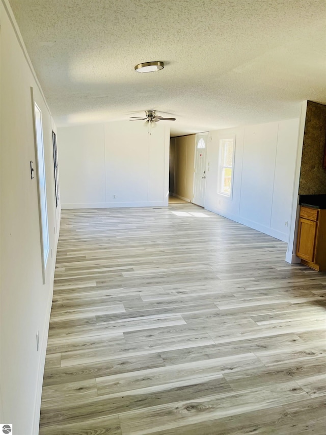 unfurnished room with a textured ceiling, ceiling fan, baseboards, and light wood-type flooring