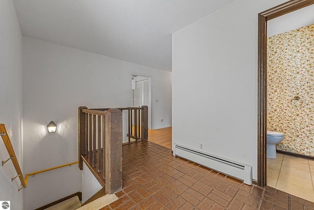 interior space with a baseboard heating unit, an upstairs landing, brick floor, and baseboards