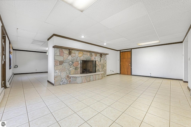 unfurnished living room featuring a baseboard radiator, a drop ceiling, ornamental molding, a stone fireplace, and baseboards
