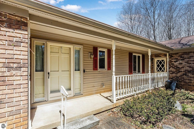 property entrance featuring brick siding, a porch, and a shingled roof