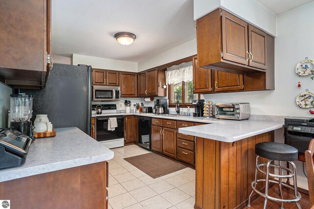 kitchen with black appliances, a peninsula, light countertops, and a sink