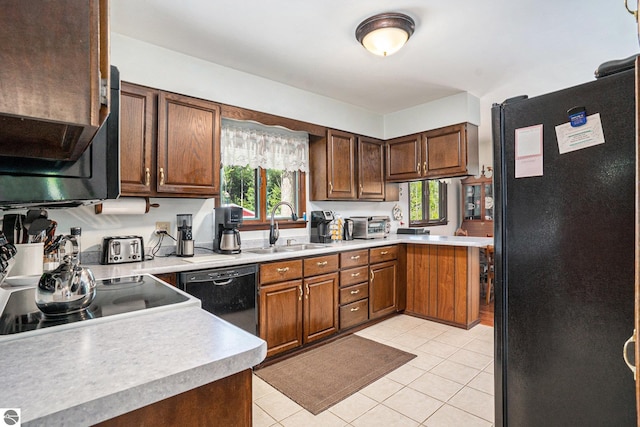 kitchen featuring a sink, light tile patterned floors, black appliances, a peninsula, and light countertops