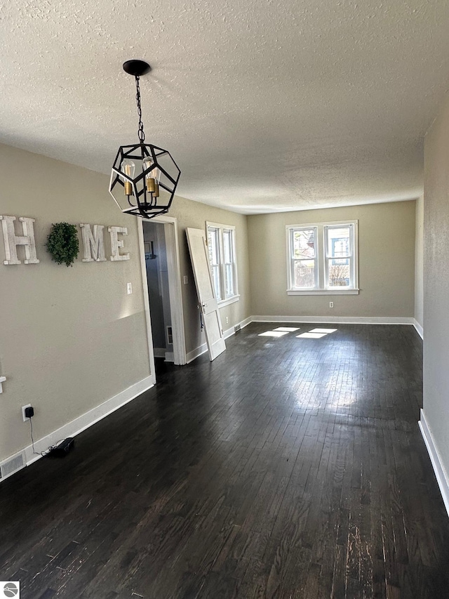 unfurnished dining area with a textured ceiling, baseboards, a chandelier, and dark wood-type flooring